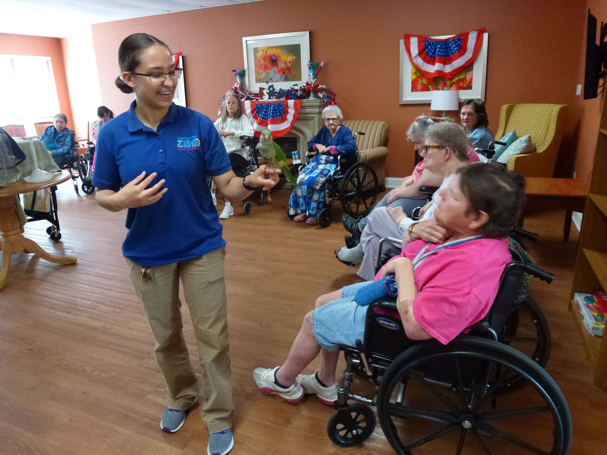 A smiling presenter holds a small, green parrot while audience members look on